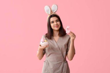 Tavşan kulaklı kadın masaj terapisti. Paskalya tavşanı ve pembe arka planda yumurtalar.