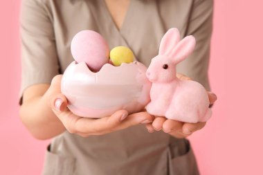 Paskalya tavşanı ve pembe arka planda yumurtaları olan kadın masaj terapisti.