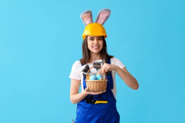 Mavi arka planda Paskalya yumurtaları olan tavşan kulaklı kadın işçi.