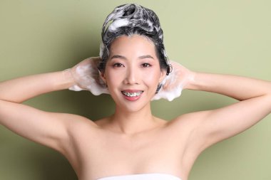 Genç Asyalı kadın yeşil arka plana şampuan sürüyor, yakın plan.