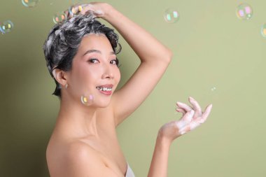 Genç Asyalı kadın yeşil arka planda şampuan ve sabun köpüğü sürüyor, yakın plan.