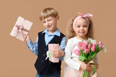 Güzel lalelerle dolu buketi ve kahverengi arka planda hediye kutuları olan şirin küçük çocuklar. Uluslararası Kadınlar Günü