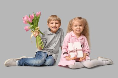 Güzel lalelerle dolu buketi ve gri arka planda hediye kutusu olan şirin küçük çocuklar. Uluslararası Kadınlar Günü