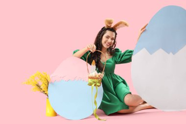 Paskalya yumurtaları pembe arka planda oturan tavşan kulaklı güzel bir kadın.