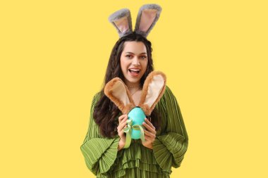 Tavşan kulaklı ve sarı arka planda Paskalya yumurtası olan güzel bir kadın.