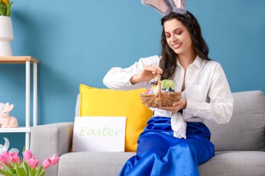 Tavşan kulaklı genç bir kadın. Paskalya sepeti evde, kanepede oturuyor.