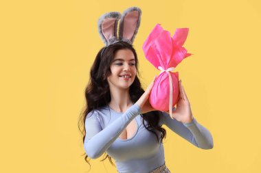 Tavşan kulaklı, sarı arka planda Paskalya hediyesi yumurtası olan genç bir kadın.