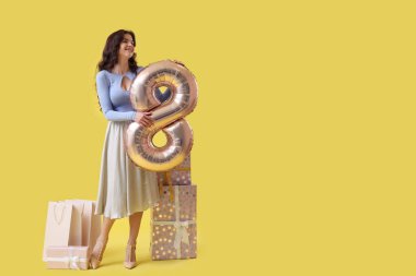 8 numaralı figür şeklinde balonu olan güzel bir kadın, sarı arka planda hediye ve alışveriş torbaları. Uluslararası Kadınlar Günü