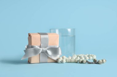 Mavi arka planda Ramazan için bir bardak su ve tespih bulunan hediye kutusu.