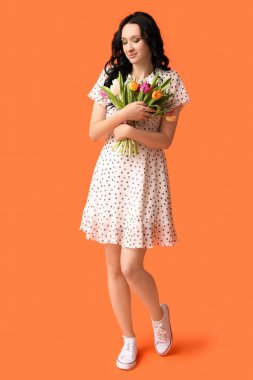 Turuncu arka planda bir buket lale ile güzel bir genç kadın. Uluslararası Kadınlar Günü