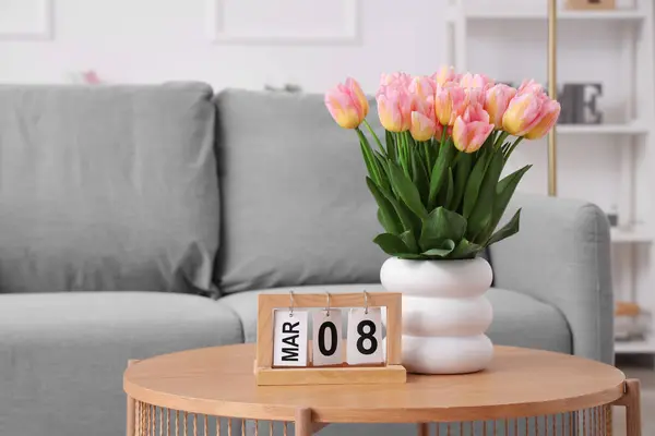 Calendar with date of International Women\'s Day and tulips on table in living room