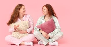 Üzerinde pijama ve pembe arka planda yastıkları olan kızıl saçlı kadınlar.