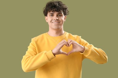 Yakışıklı genç adam, elleri yeşil arka planda kalp yapıyor.