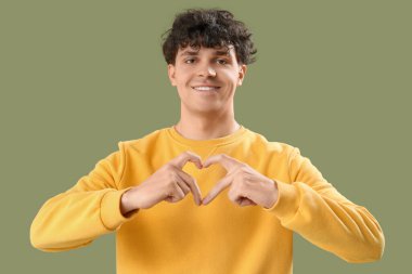 Yakışıklı genç adam, elleri yeşil arka planda kalp yapıyor.