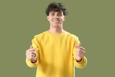 Yakışıklı genç adam yeşil arka planda parmaklarıyla kalp yapıyor.