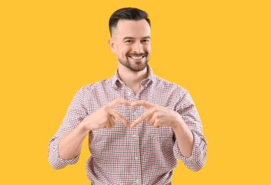 Yakışıklı adam, elleri sarı arka planda kalp yapıyor.