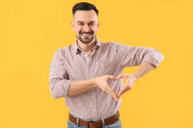 Yakışıklı adam, elleri sarı arka planda kalp yapıyor.