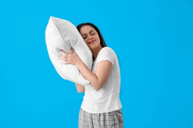 Mavi arka planda yumuşak yastıklı mutlu genç kadın