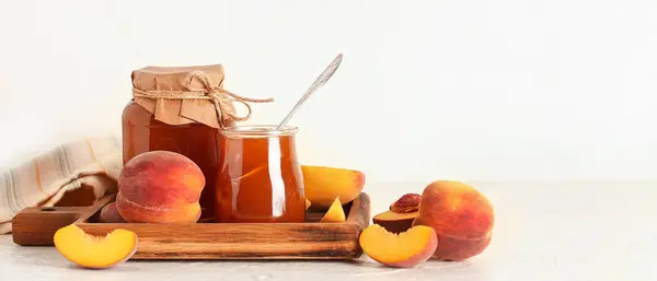 Jars with sweet peach jam on light background with space for text