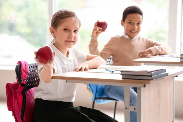 Little students with apples sitting at desks in classroom