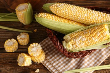 Tahta arka planda taze mısır koçanları olan sepet.