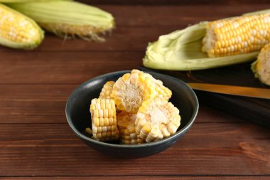 Tahta arka planda kesilmiş taze mısır koçanı ile kase