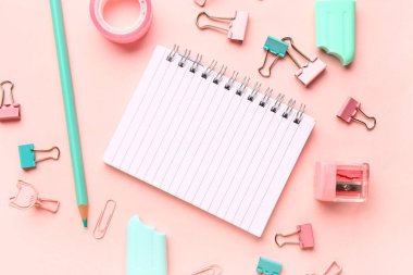 Pembe arka planda farklı kırtasiye malzemesi içeren defter.