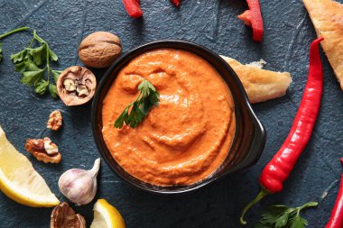 Bir kase lezzetli muhammara ve siyah arka planda malzemeler.