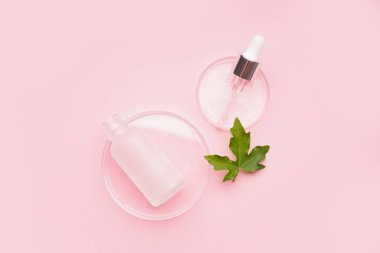 Pembe arka planda bitkilerle ve bir şişe kozmetik ürünlerle dolu petri kapları.