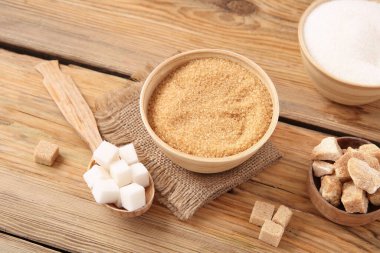 Tahta arka planda farklı tipte şeker bulunan kaseler ve kaşıklar.