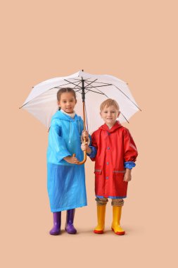 Bej arka planda şemsiyesi olan lastik çizmeli küçük çocuklar.