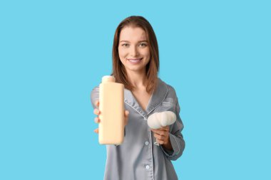 Mavi arka planda banyo jeli ve lifli pijamalı güzel bir kadın.