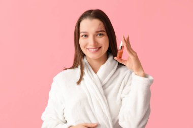 Pembe arka planda serumu olan bornozlu güzel bir kadın.