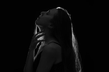 Siyah arka planda boynuna dokunan genç bir kadının silüeti, yakın plan.