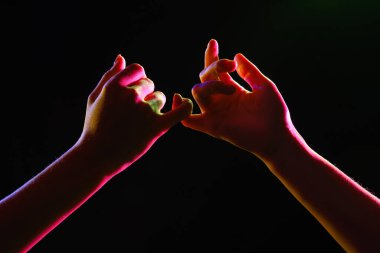 Küçük parmaklarını karanlık arka planda tutan kadın silueti, yakın plan.