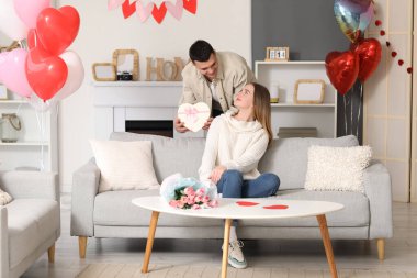 Hediye kutusu, çiçek buketi ve evde Sevgililer Günü 'nü kutlayan kalp şeklinde balonları olan genç ve güzel bir çift.