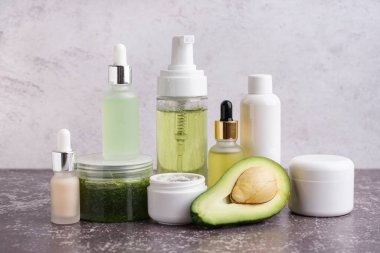 Taze avokado, gerekli yağ şişeleri ve renk arka planında farklı kozmetik ürünler.