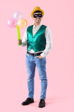 Kostümlü ve karnaval maskeli mutlu genç adam pembe arka planda balonlardan yapılmış bir buket