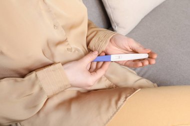 Hamilelik testi olan bir kadın evdeki kanepede oturuyor.