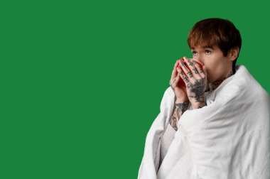 Battaniyeli yakışıklı genç adam yeşil arka planda çay içiyor.