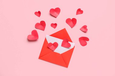 Zarflı kompozisyon, kart ve pembe arka planda kırmızı kağıt kalpler. Sevgililer Günü kutlaması