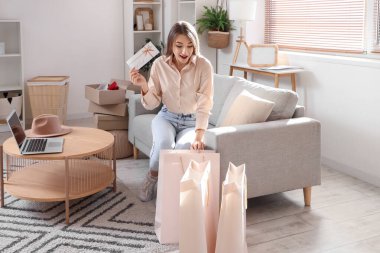 Evde hediye kartı ve alışveriş torbalarıyla genç bir kadın var.