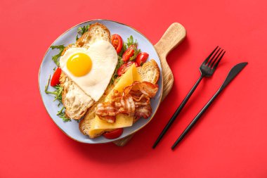 Lezzetli kızarmış yumurta, kruvasan, pastırma, domates, roka ve kırmızı arka planda roka.