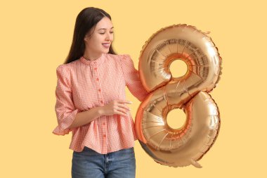 Sarı arka planda 8 numaralı figür şeklinde altın renkli hava balonu olan güzel bir Asyalı kadın. Uluslararası Kadınlar Günü