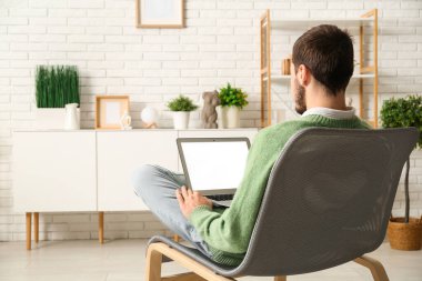 Evde online randevuda dizüstü bilgisayar kullanan yakışıklı genç adam.