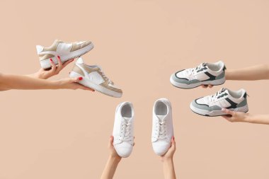 Bej arka planda farklı spor ayakkabıları tutan kadın eller.