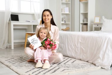 Küçük kız, mutlu annesini bir buket güzel çiçek ve tebrik kartıyla kutluyor. Anneler Günü kutlaması
