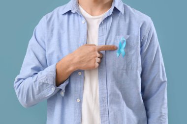 Genç adam mavi kurdeleyi işaret ediyor. Renkli arka plan, yakın plan. Prostat kanseri farkındalığı