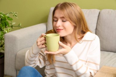 Evde bir fincan çayla dinlenen genç bayan.