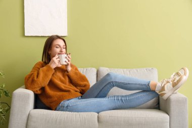 Evdeki kanepede çay içen genç bir kadın.